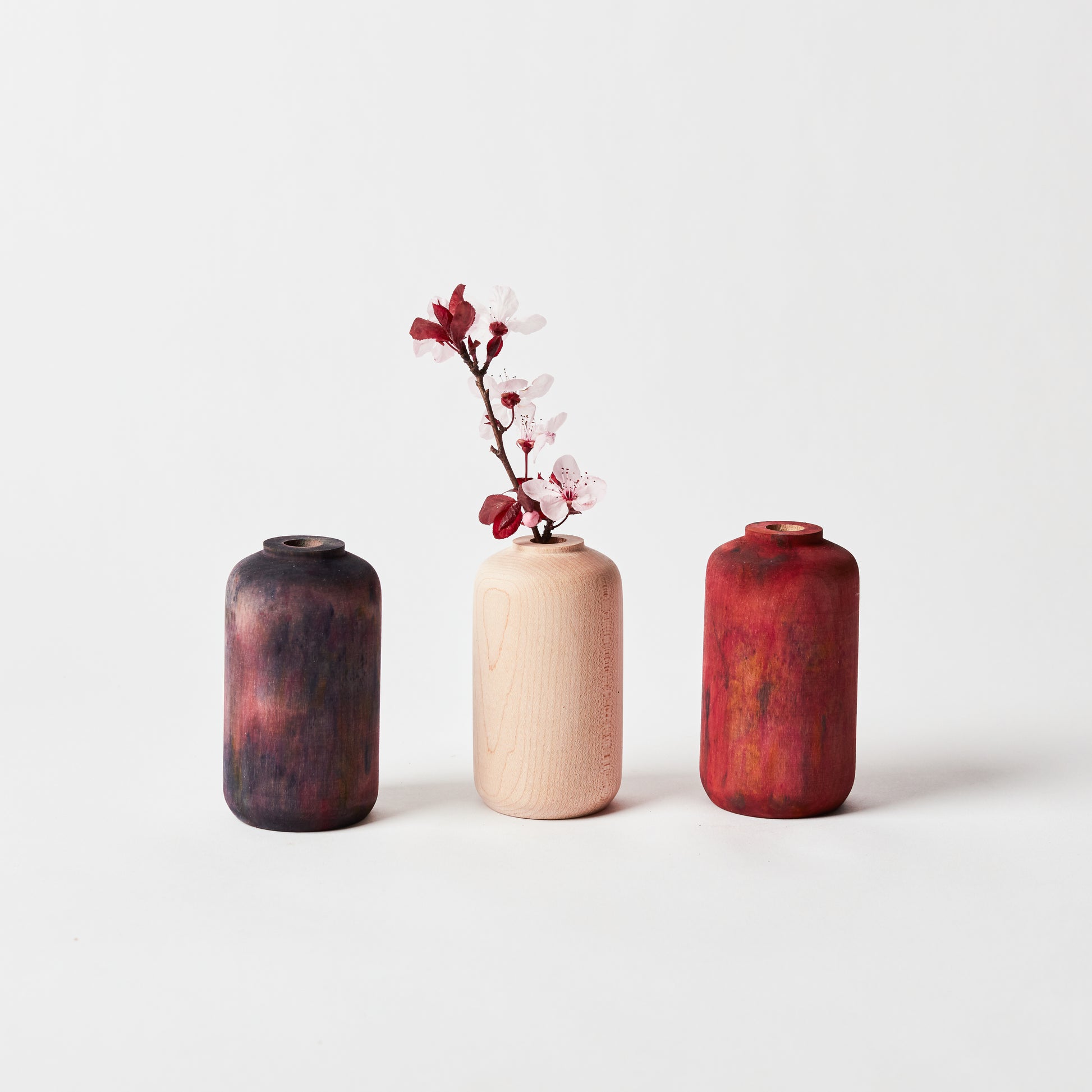 Left to Right: Midnight maple bud vase, undyed maple bud vase holding flowers, crimson maple bud vase.