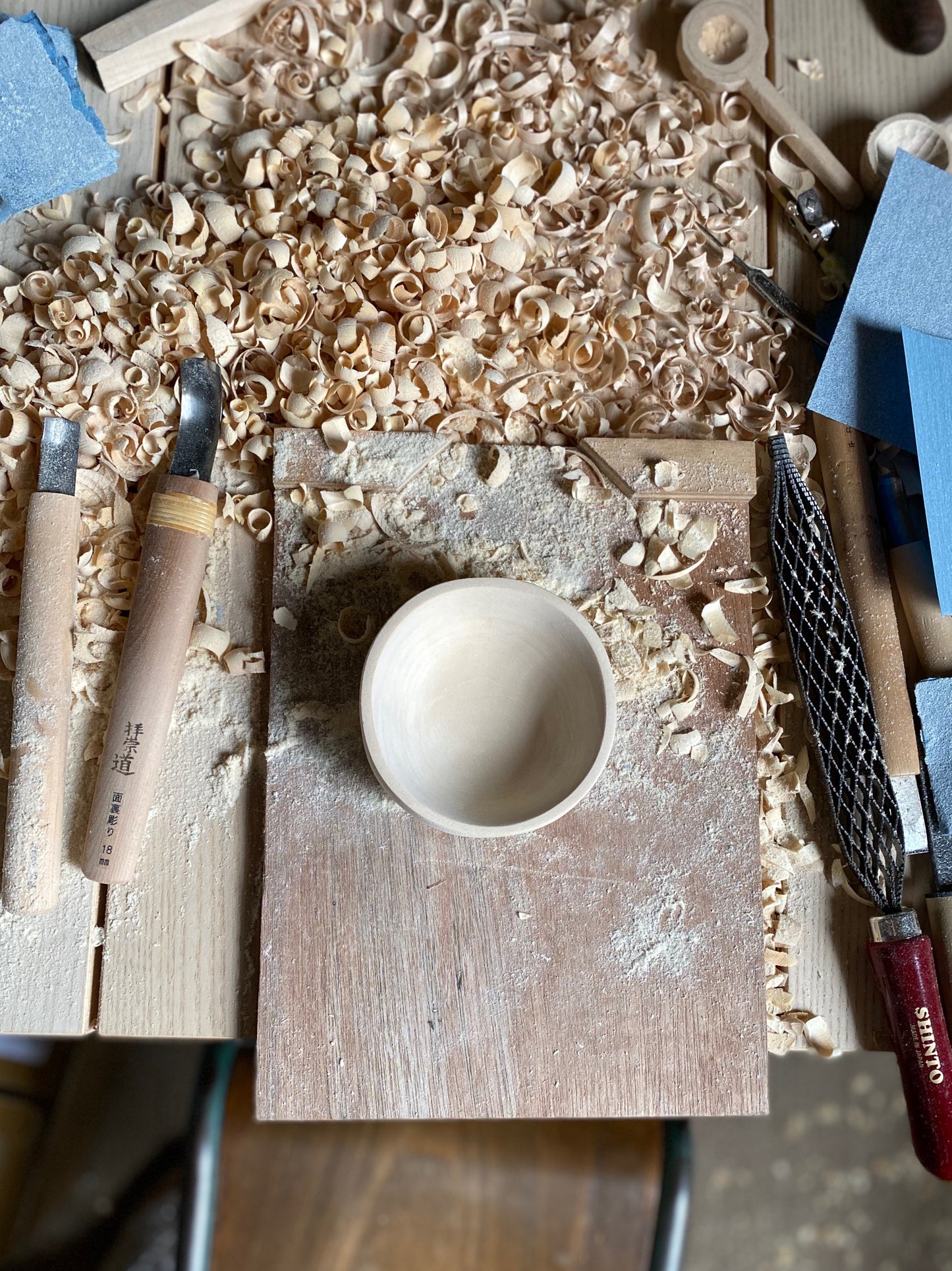 Aerial view of the finished bowl piece on a bench hook with wood shavings and tools all around. By Melanie Abrantes Designs.