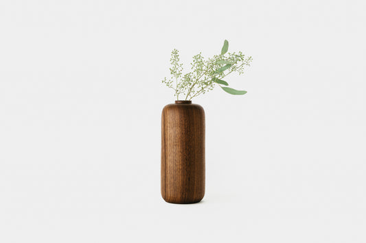 Tall bud vase made of walnut, holding plant. By Melanie Abrantes Designs.