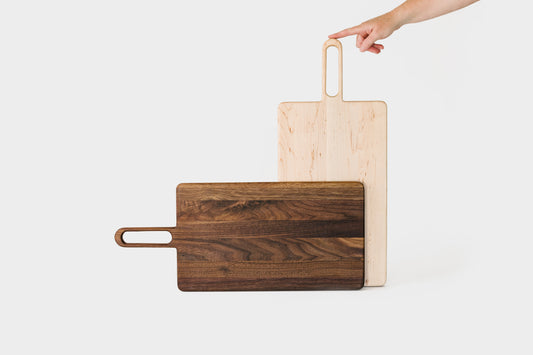 Big Bread Board shown in Walnut and Maple. The handle has a simple but fun design with a cut out in the middle.