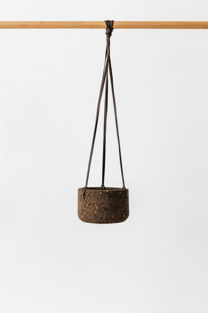Small charcoal cork hanging planter with a dark brown leather lace, shown hanging on a pole.