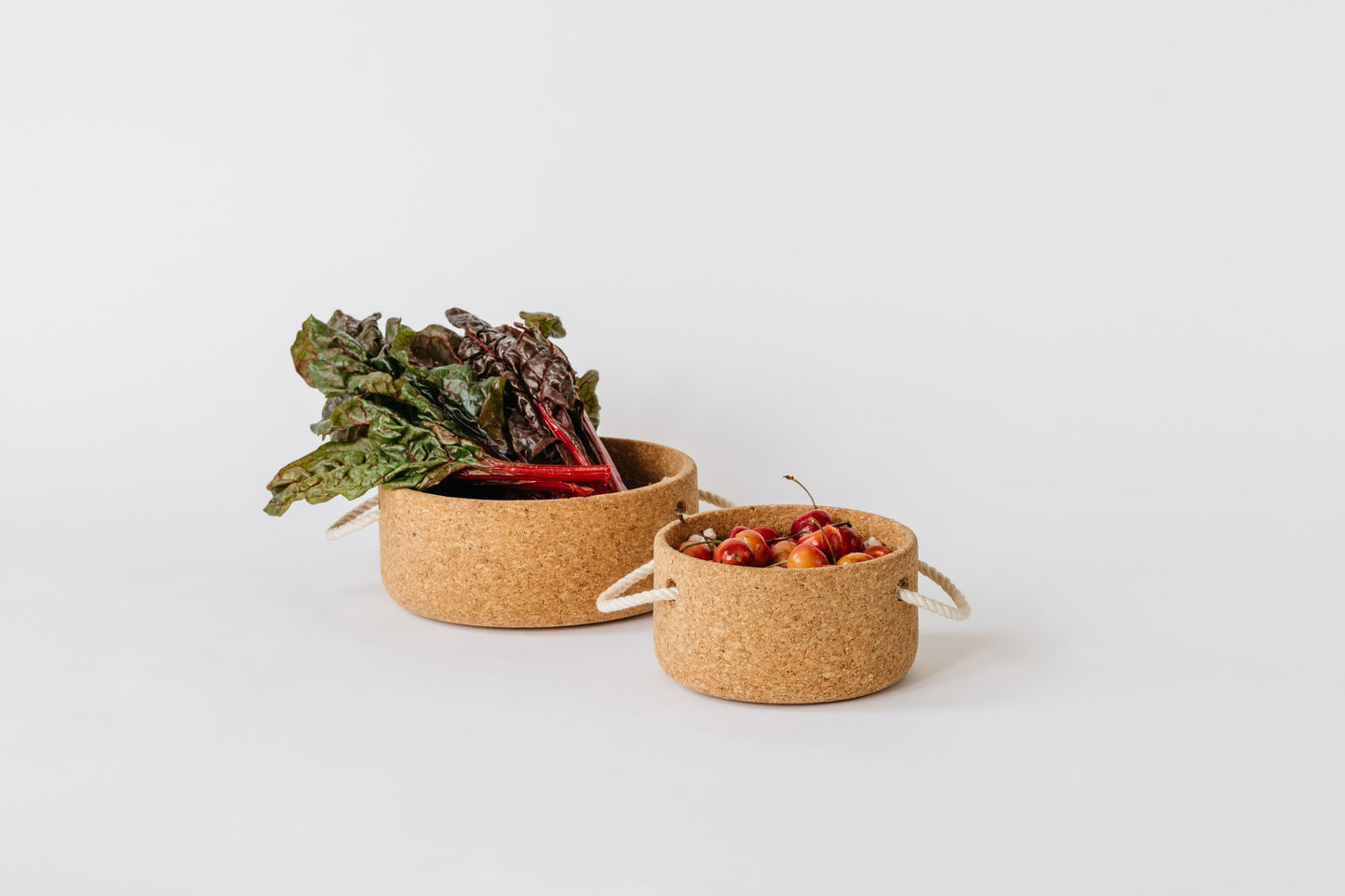 Large cork bowl with greens and small cork bowl filled with cherries. By Melanie Abrantes Designs.