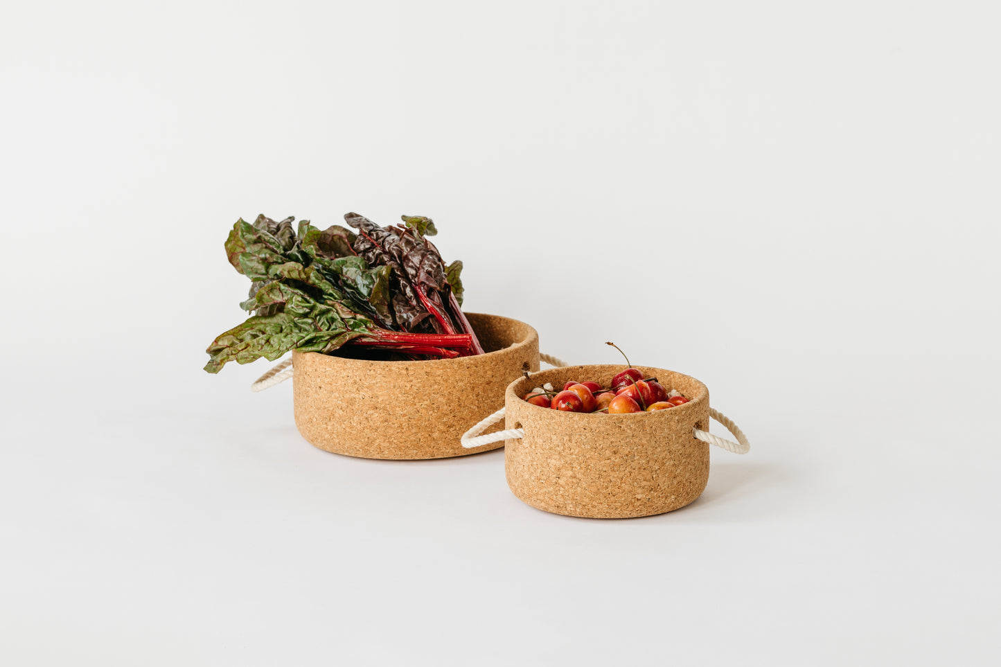 Large cork bowl with greens and small cork bowl filled with cherries. By Melanie Abrantes Designs.