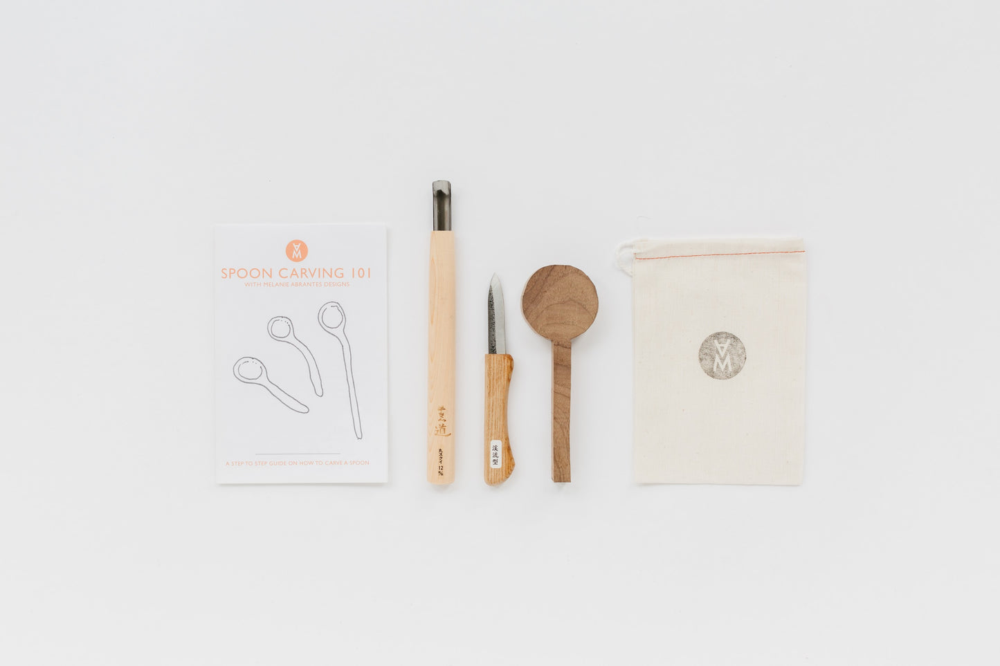 Spoon carving instructions, spoon gouge, carving knife, walnut spoon blank, and a canvas bag laid out. By Melanie Abrantes Designs.