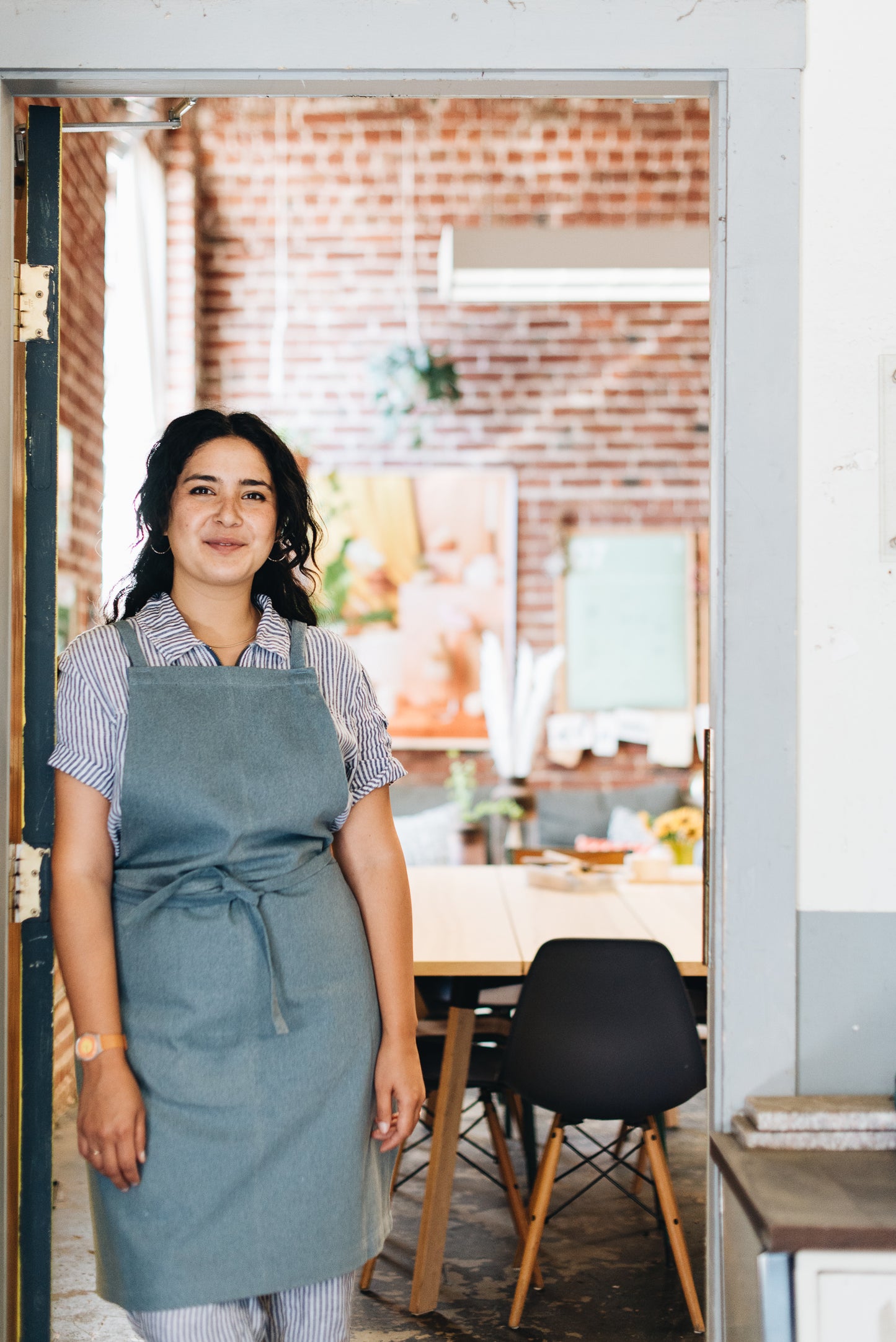 GDS Studio Apron Collaboration on Melanie Abrantes. Apron worn, standing in doorway.