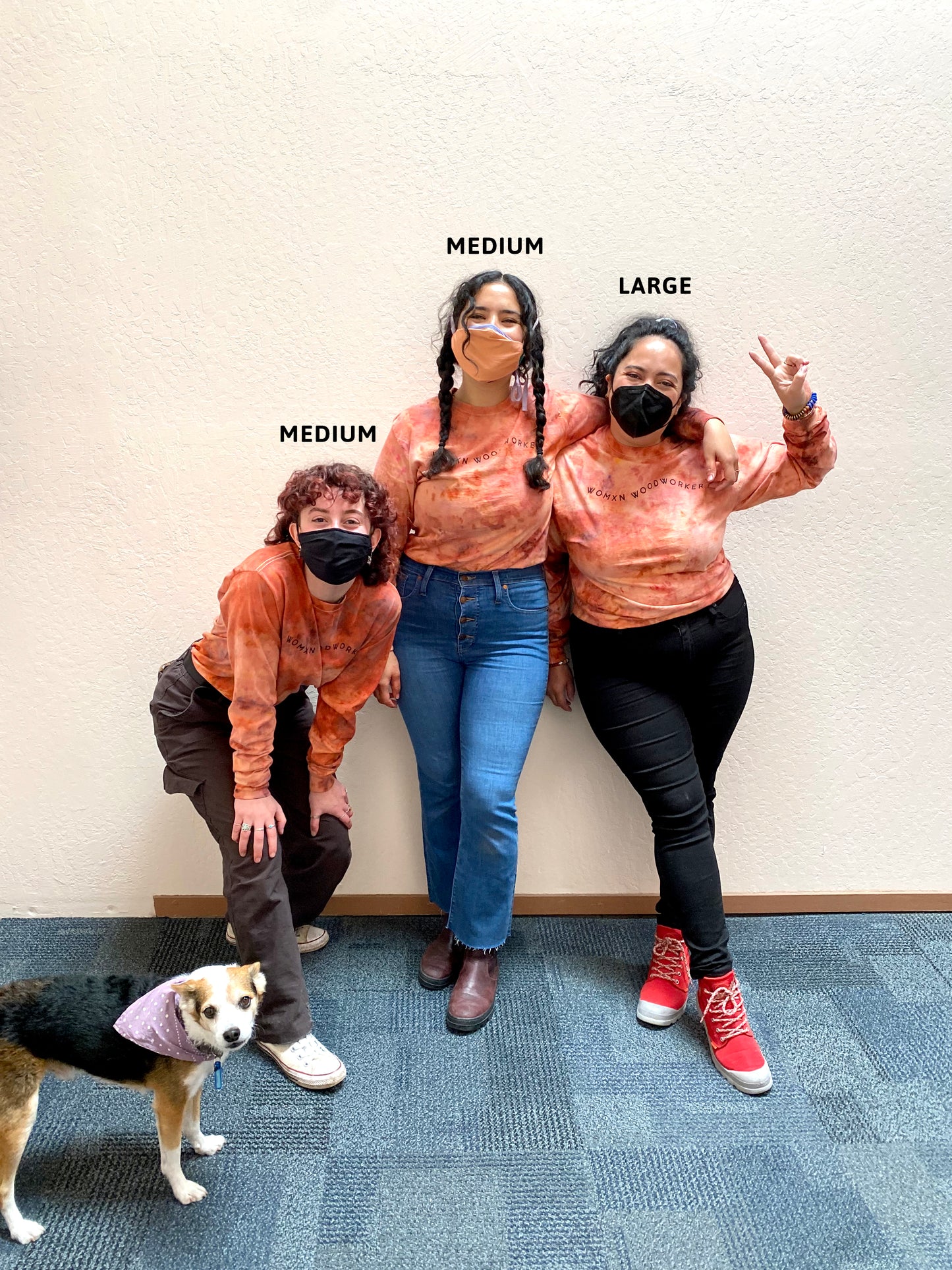 Dog and three people wearing Womxn Woodworker sweatshirts. Left to right reads "Medium, Medium, Large"