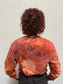 Person with red curly hair wearing tie-dye crimson and orange sweatshirt. Reads "Mels Carving Club / Oakland California" in black font.