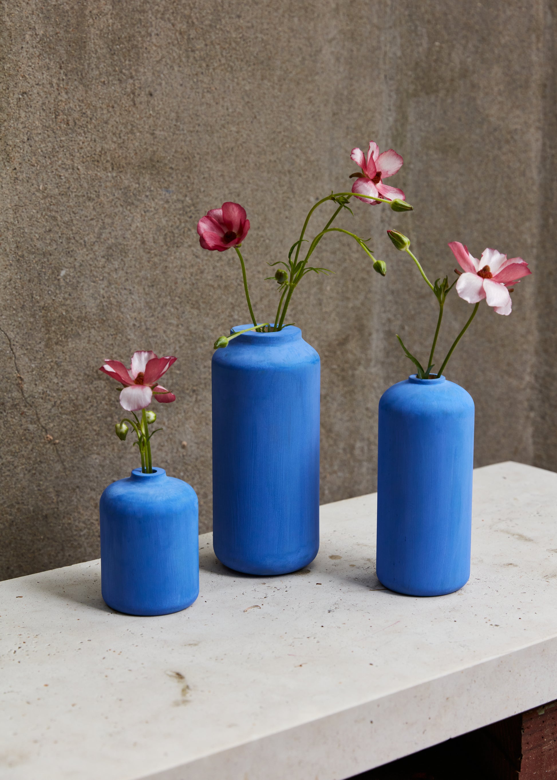 All three cobalt blue bud vases on a marble slab with a grey background. Purple flowers in the vases. By Melanie Abrantes Designs