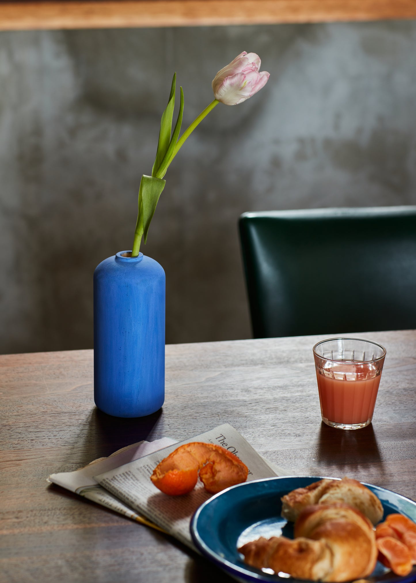 Tall bud vase in cobalt blue with lily flower. Set on a wood table with a morning breakfast. By Melanie Abrantes Designs.