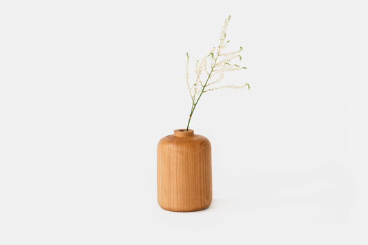 Straight bud vase made from a solid piece of cherry wood. Displayed with a little greenery.