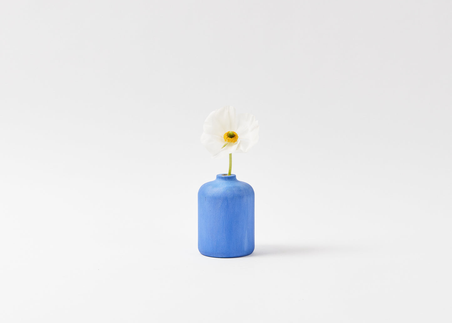 Hand painted bud vase in cobalt blue with a white flower inside the vase. By Melanie Abrantes Designs