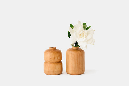 Double bud vase on the left, straight bud vase on the right with a white flower.  Both made of cherry wood. By Melanie Abrantes Designs.