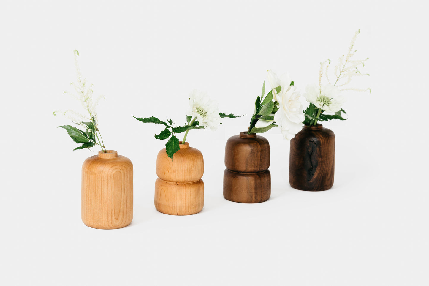 Collection of cherry and walnut bud vases in different styles, all holding flowers. By Melanie Abrantes Designs.