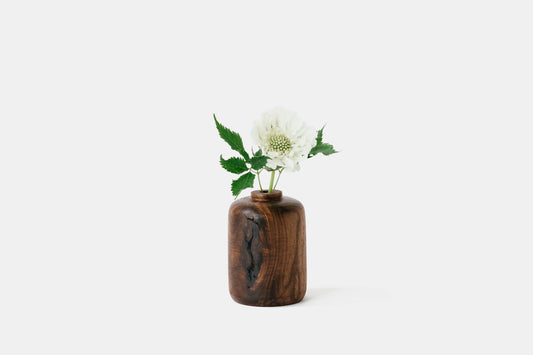 Walnut wood bud vase holding a white flower. By Melanie Abrantes Designs.