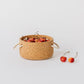 Natural cork basket with white rope handles. Filled with cherries. Made by Melanie Abrantes Designs.