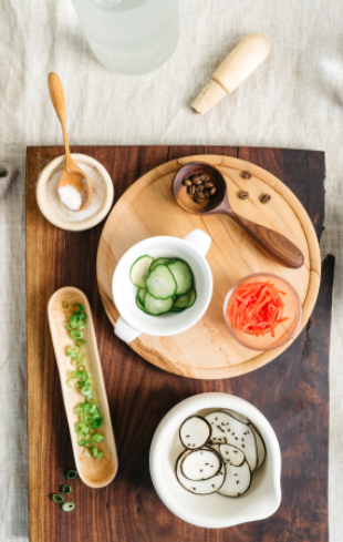 Finished spoon being used in a salt bowl and the other with coffee beans. Displayed with other food on a cutting board.